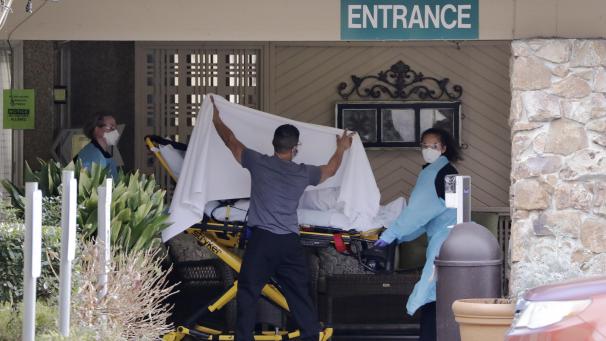 <p>USA, Kirkland: Ein Mitarbeiter verdeckt eine Person, die auf einer Bahre zu einem wartenden Krankenwagen vor einer Pflegeeinrichtung gebracht wird.</p>