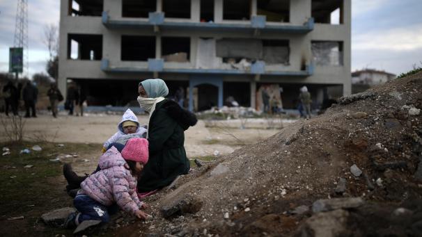 <p>Eine Migrantin sitzt mit zwei Kindern an einem Erdhaufen vor einem verlassenen Gebäude nahe der türkisch-griechischen Grenze. An der ostgriechischen Grenze zur Türkei bleibt die Lage angespannt.</p>