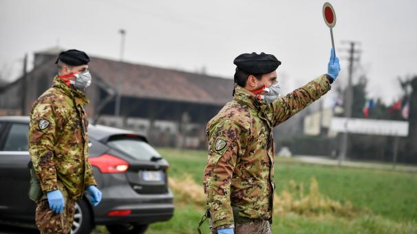 <p>Ein Soldat mit Atemschutzmaske hält an einer Straßensperre vor der roten Zone von Turano Lodigiano eine Winkerkelle in die Höhe.</p>