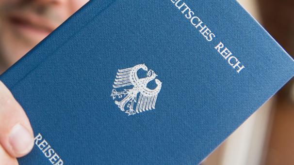 <p>Ein Mann hält ein Heft mit dem Aufdruck „Deutsches Reich - Reisepass“ in der Hand</p>