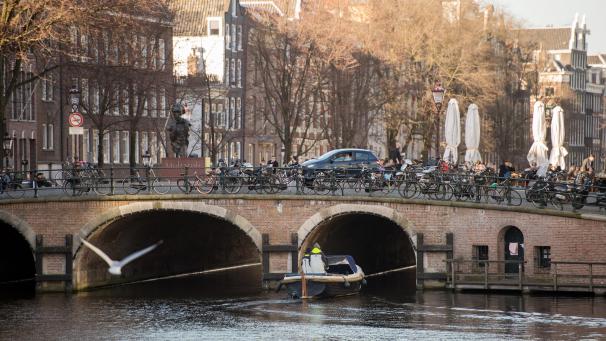 <p>Amsterdam: Ein Boot fährt auf einer Gracht unter einer Brücke hindurch.</p>