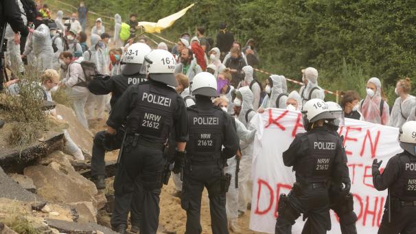 <p>Umweltaktivisten im weißen Overalls klettern am 25. Juli über ein Wall um in dem Tagebau Garzweiler einzudringen und werden von der Polizei zuruckgewiesen.</p>