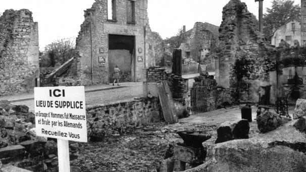 <p>Blick auf die Ruinen von Oradour-sur-Glane (Frankreich) und eine Gedenktafel, deren Text lautet: „Gedenkstätte - Eine Gruppe von Männern wurde hier von den Deutschen massakriert und verbrannt - Besinnt Euch.“</p>