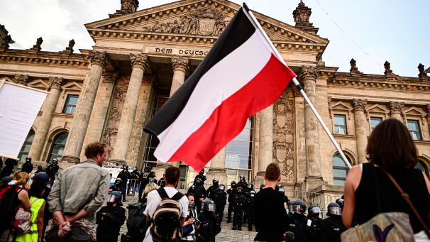 <p>Teilnehmer einer Kundgebung gegen die Corona-Maßnahmen stehen vor dem Reichstag, ein Teilnehmer hält eine Reichsflagge.</p>