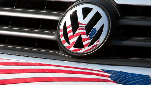 <p>Die US-Fahne spiegelt sich in Logo und Kühlergrill eines Volkswagen-Fahrzeugs. Der Beginn der „Dieselgate“-Affäre jährt sich in dieser Wochen zum fünften Mal.</p>
