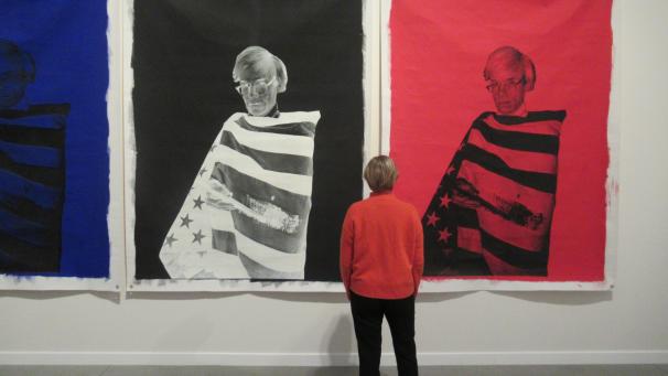 <p>Eine Besucherin steht vor den Arbeiten „Andy in American flag“ von Christopher Makos (1982).</p>