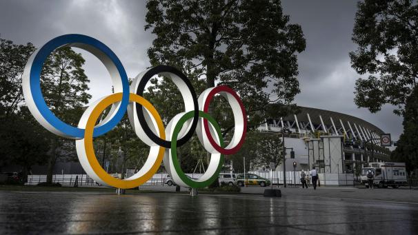 <p>Ein Monument mit der Darstellung der Olympischen Ringe leuchtet vor dem Nationalstadion in Tokio unter dunklen Wolken.</p>