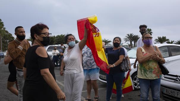 <p>Anwohnerinnen und Anwohner protestieren mit einer spanischen Flagge gegen eine Demonstration für die Rechte von Migranten.</p>