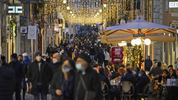 <p>Zahlreiche Menschen mit Mund-Nasen-Schutz gehen eine weihnachtlich geschmückte Einkaufsstraße in einer italienischen Innenstadt entlang.</p>