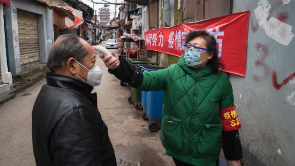 <p>Eine Gemeindemitarbeiterin misst die Körpertemperatur eines Passanten in Wuhan, Anfang Februar 2020.</p>