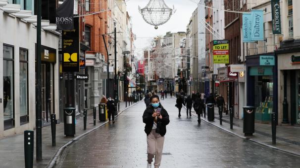 <p>Passanten mit Mund-Nasen-Bedeckungen gehen über die sonst geschäftige Grafton Street in Dublin.</p>