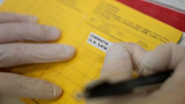 <p>Ein Mitglied eines Mobilen Impfteams klebt in einem Altenpflegeheim nach einer Impfung einen Aufkleber in einen Impfausweis.</p>