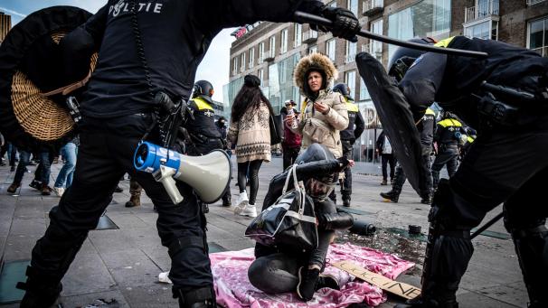 <p>Zwei Polizisten beugen sich über eine Demonstrantin, die auf einer Straße sitzt. Mehrere hundert Menschen haben vor dem Bahnhof von Eindhoven gegen die aktuelle Corona-Politik demonstriert.</p>