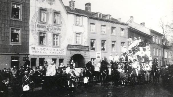 <p>Prinz Johann I. (Frings) wird Karneval 1908 im offenen Landauer zum Restaurant Kreusch auf der Klötzerbahn gebracht. Mit ihm in der Kutsche fährt der 1. Vorsitzende des Komitees, Zigarrenfabrikant Alfred Koch (mit hellem Zylinder). Davor stehen die ersten Blauen Funken als Wache. Rechts der Wagen der Harmonie-Musikvereinigung und davor die Herolde des Prinzen.</p>