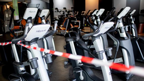 <p>Ein rot-weißes Flatterband ist an Fahrradtrainern befestigt, die in einem Fitnessstudio stehen.</p>