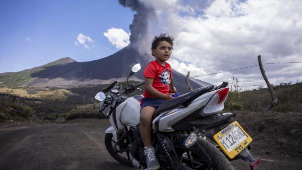 <p>Ein Kind sitzt auf einem Motorrad, während im Hintergrund der Vulkan Pacaya ausbricht.</p>