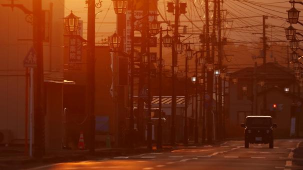 <p>Ein Fahrzeug fährt auf einer menschenleeren Straße in der Präfektur Fukushima. Die Stadt Namie in der Nähe des lahmgelegten Kernkraftwerks Fukushima Daiichi ist auch fast 10 Jahre nach dem Erdbeben menschenleer und der Zugang noch immer eingeschränkt.</p>