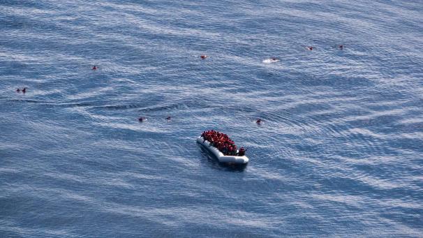 <p>Migranten sitzen in einem Schlauchboot vor der Küste Libyens, während einige im Wasser schwimmen.</p>