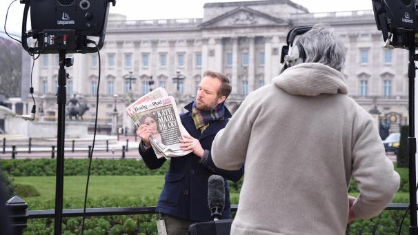 <p>Der CBS-Berichterstatter Ian Lee steht vor dem Buckingham Palace und hält eine Zeitung, auf der die Schlagzeile „Kate made me cry““ neben einem Foto von Herzogin Meghan zu lesen ist.</p>