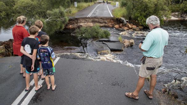 <p>Menschen stehen an einem unterspülten Straßenabschnitt 200 Kilometer nördlich von Sydney.</p>