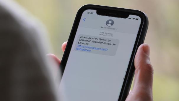 <p>Eine Frau hält ein Smartphone in ihrer Hand, auf dessen Display eine Betrugs-SMS zu lesen ist. Beim sogenannten Smishing setzen Kriminelle darauf, dass Verbraucher auf den mitgeschickten Link klicken und sich in einem nächsten Schritt unwissentlich eine Schadsoftware runterladen.</p>