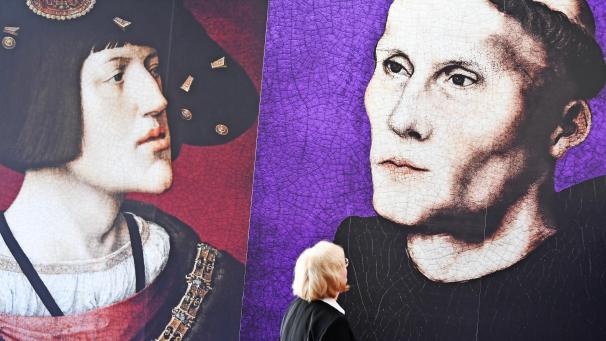 <p>Eine Frau steht in der Ausstellung „Luther in Worms 1521 - Der Ort des Geschehens“ vor Bildern von Martin Luther (rechts) und König Karl dem Fünften.</p>