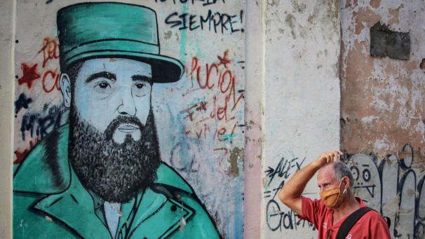 <p>Ein Mann mit Mund-Nasen-Schutz geht vor einem Wandbild des ehemaligen kubanischen Präsidenten Fidel Castro.</p>