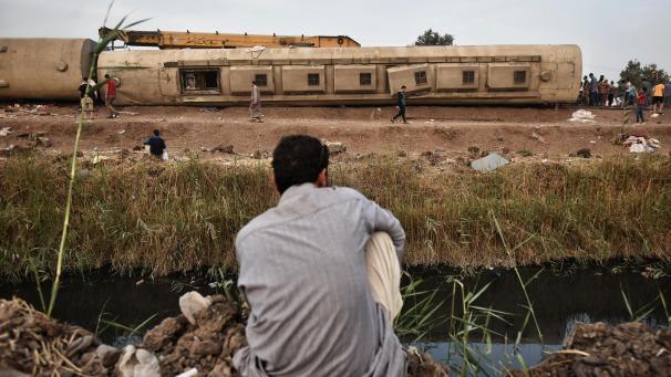 <p>Ein Mann blickt auf die Unfallstelle mit beschädigten Waggons eines Personenzugs.</p>