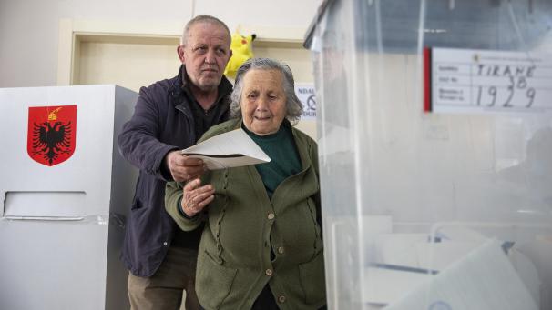 <p>Ein Mann hilft einer älteren Frau dabei, ihren Stimmzettel in eine Wahlurne zu werfen.</p>