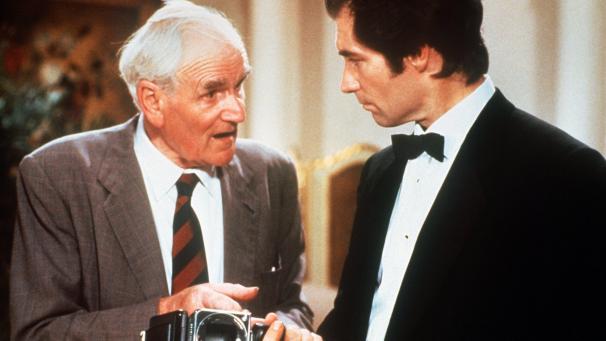 <p>Timothy Dalton (r.) als James Bond hält eine Kamera in der Hand, die gleichzeitig eine Signaturwaffe ist, im Gespräch mit Desmond Llewelyn als Geheimwaffenerfinder „Q“ in einer Filmszene (Archivfoto von 1989).</p>