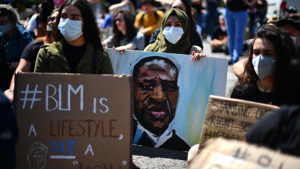 <p>Eine Frau (M.) hält ein Gemälde mit der Abbildung von George Floyd.</p>