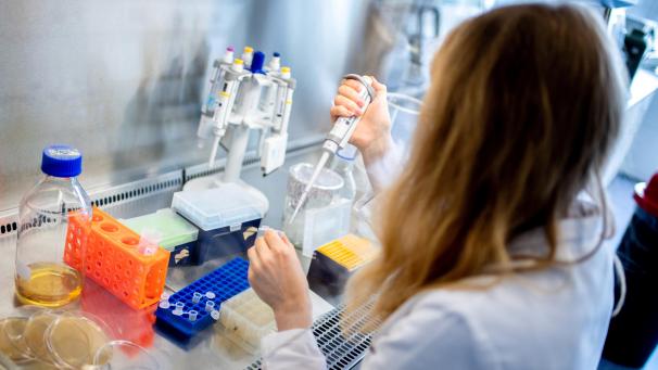 <p>Eine wissenschaftliche Mitarbeiterin überprüft in einem sterilen Bereich selektierte Antikörper mit einer Pipette.</p>