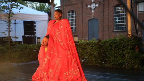 <p>Drei Tanzende der Tschepko Dance Company stecken unter einem Mantel.</p>