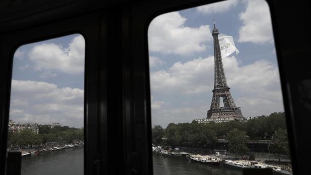 <p>Durch ein Fenster der Hochbahn ist der Pariser Eiffelturm zu sehen, an dem eine riesige weiße Fahne weht.</p>