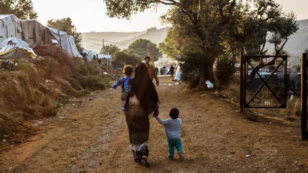 <p>Ein Frau geht mit einem Kind auf dem Arm und einem anderen Kind an der Hand auf einem Weg im Flüchtlingslager Moria auf der griechischen Insel Lesbos. Im September 2020 kam es durch Brandstiftung seitens mehrerer junger Migranten aus Afghanistan zu einem Großbrand, der das Lager und die Habe der Flüchtlinge fast vollständig zerstörte und 12.600 Menschen obdachlos machte.</p>