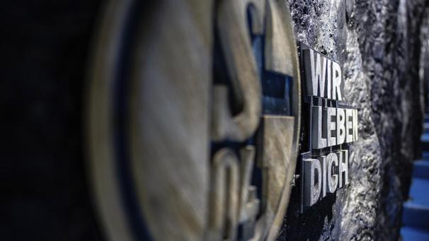 <p>Im Spielertunnel hängt an einer nachgebauten Kohlewand das Logo des FC Schalke 04 mit dem Schriftzug: „Wir leben Dich“.</p>
