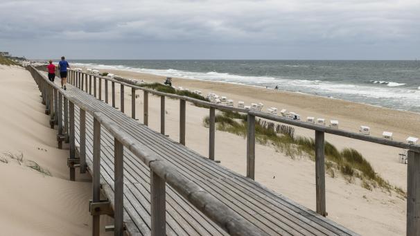 <p>Ein Mann und eine Frau joggen bei bewölktem Himmel am Strand von Westerland.</p>