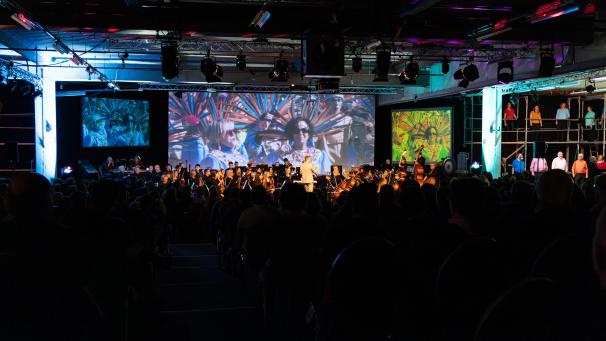 <p>Das Orchester spielt, während auf der großen Leinwand die Geschichte der Welt und Ostbelgiens präsentiert wird.</p>