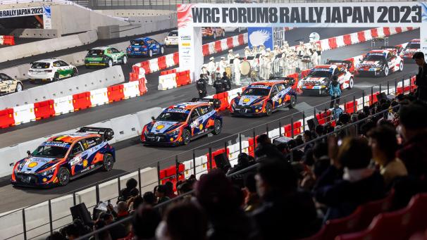 <p>Startzeremonie der Rallye Japan im Stadion, links Neuvilles Auto.</p>