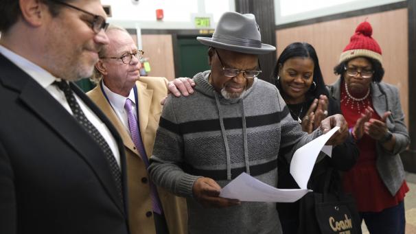 <p>Glynn Simmons (Mitte) liest den Gerichtsbeschluss, während seine Anwälte Joe Norwood und John Coyle (links) und seine Nichten Cecilia Hawthorne und Madeline Jones (rechts) zuschauen.</p>