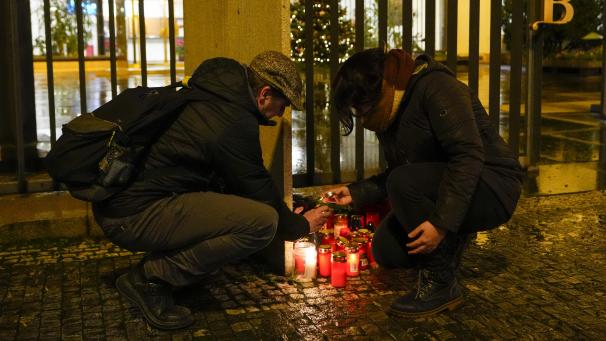 <p>Zwei Personen entzünden Kerzen vor dem Gebäude der Philosophischen Fakultät der Karls-Universität in der Prager Innenstadt.</p>