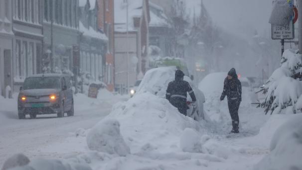 <p>Menschen stehen bei heftigen Schneefall hinter einem zugeschneiten Auto in Kristiansand.</p>