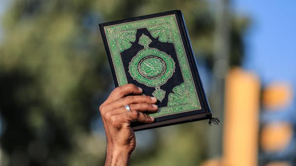 <p>Ein Mann hält ein Exemplar des Koran hoch.</p>