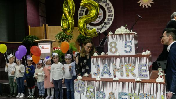 <p>Eine große Torte aus Pappe bringen die Kindergartenkinder auf die Bühne der Gemeindeschule.</p>