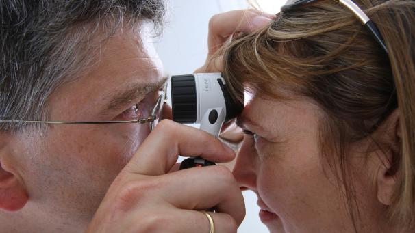 <p>Ein Hautarzt untersucht in seiner Praxis mit einem Vergrößerungsglas die Haut einer Patientin bei einer Hautkrebs-Früherkennung.</p>