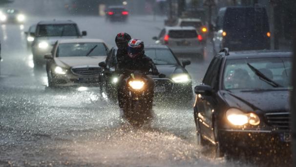 <p>Autos und Motorräder fahren bei starkem Regen über eine überflutete Straße.</p>