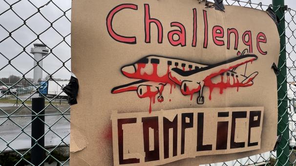 <p>Ein Protest-Plakat hängt an einem Zaun des Lütticher Regionalflughafens.</p>