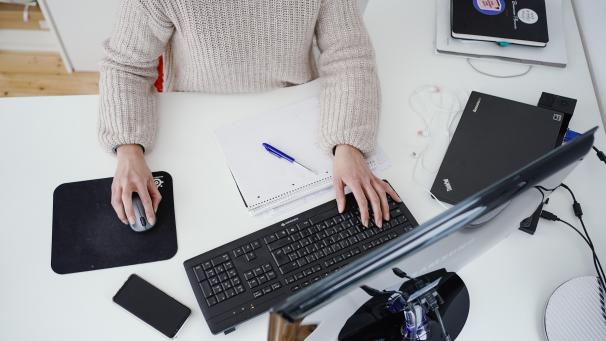 <p>Eine Frau arbeitet in ihrer Wohnung vor einem Computer an einem Stehtisch.</p>