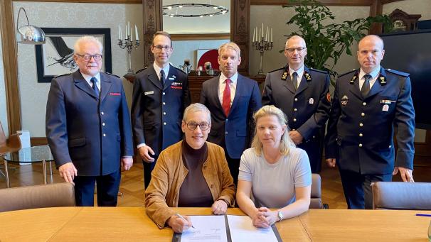 <p>Sibylle Keupen und Claudia Niessen bei der Unterzeichnung der Vereinbarung zur grenzüberschreitenden Hilfeleistung. Im Hintergrund sind Peter Sellung, Leiter der Stabsstelle Internationale Zusammenarbeit, Andreas Bierfert, Fachbereichsleiter Feuerwehr und Rettungsdienst, Feuerwehrdezernent Dr. Markus Kremer, Francis Cloth, Kommandant der Hilfeleistungszone der DG, sowie René Schoonbrood, Direktor des Risikomanagements der Hilfeleistungszone der DG, zu sehen.</p>