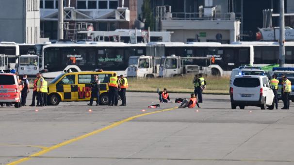 <p>Einsatzfahrzeuge von Polizei, Feuerwehr und Flughafen-Sicherheit stehen auf dem Vorfeld des Frankfurter Flughafens, wo sich zwei Aktivisten (m.) festgeklebt haben.</p>
